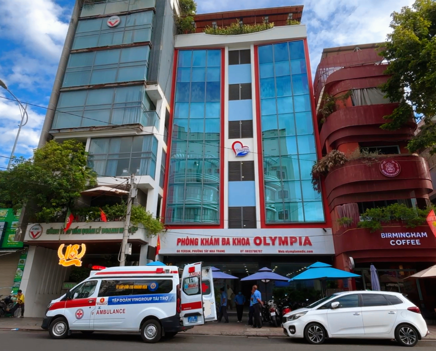 Xe cấp cứu 115 Khánh Hòa với cửa sau mở, đỗ trước cổng Phòng khám Đa khoa Olympia
